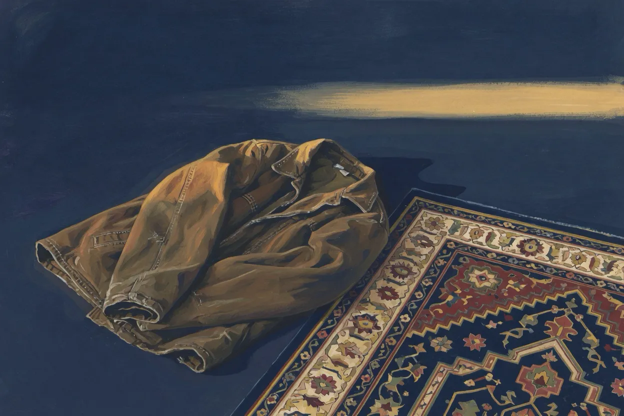 A folded work jacket beside the corner of a prayer rug in late gold light.